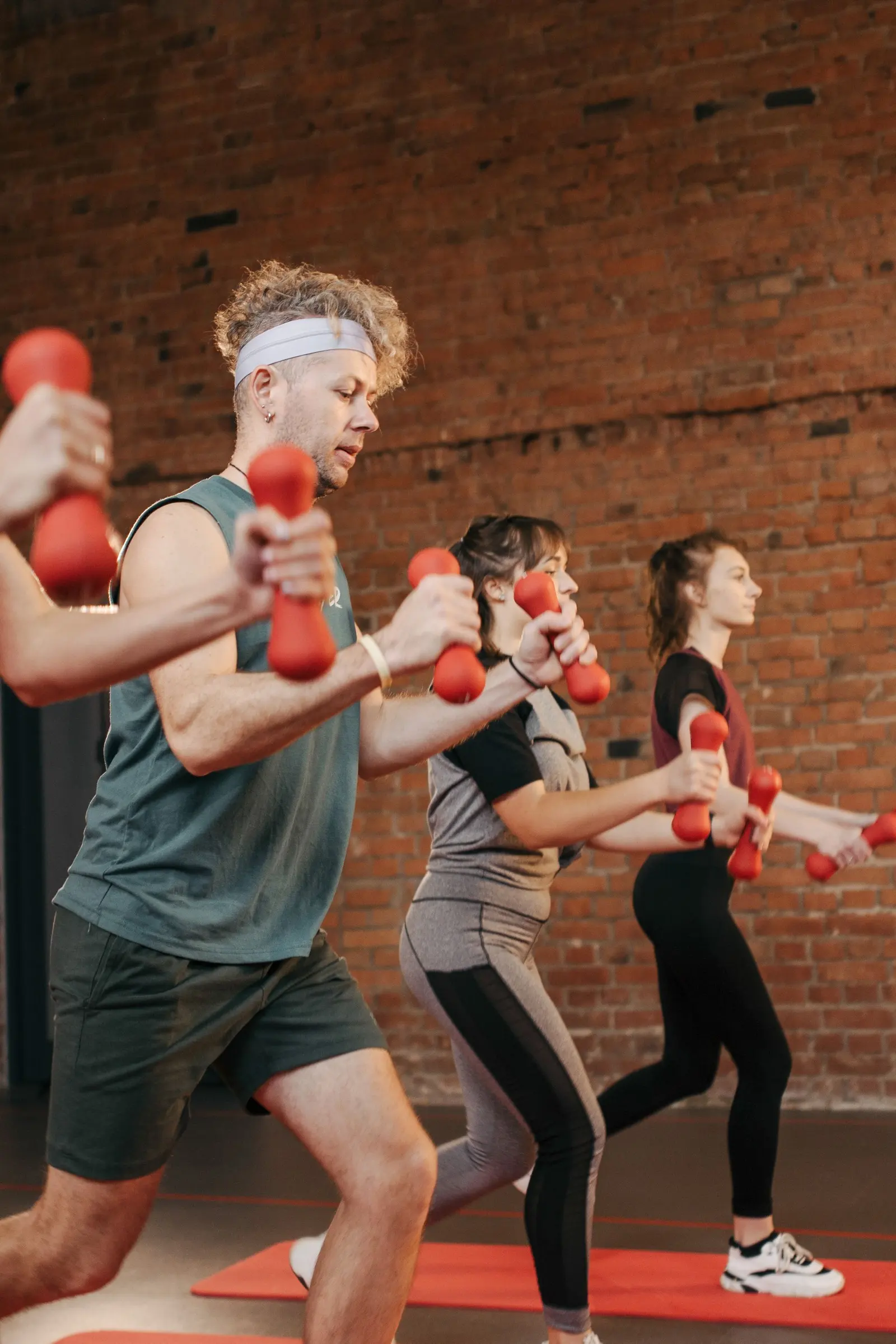 Group class lifting light dumbbells together in a brick-walled studio